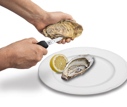 Oyster knife opening an oyster by hand over plate with lemon slice